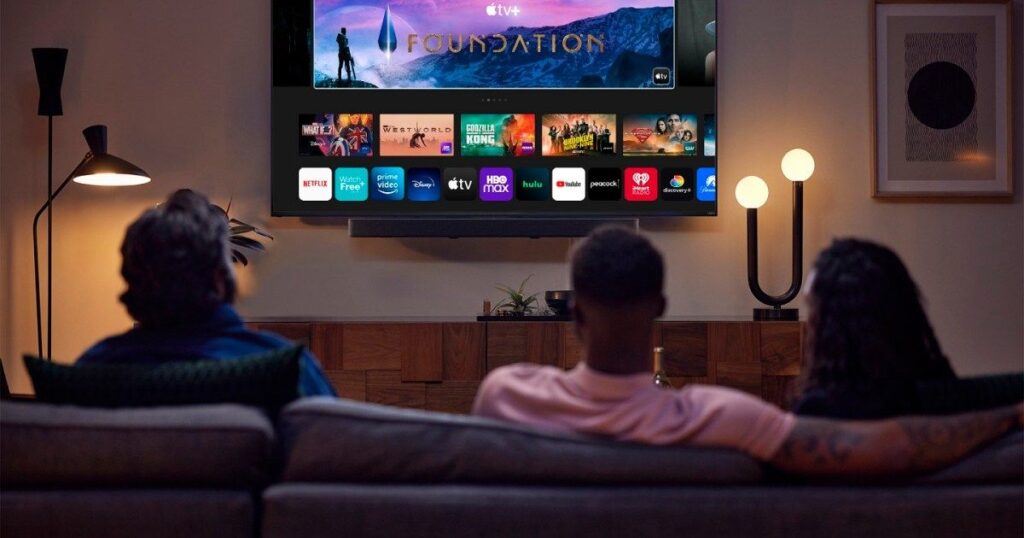 An excited fan watching a live football game on multiple screens—a large living room TV, a tablet, and a smartphone—showcasing the flexibility of IPTV streaming